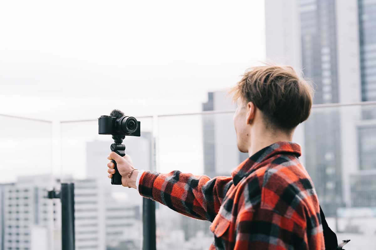 Vlogger using ZV-E10 on shooting grip overlooking city