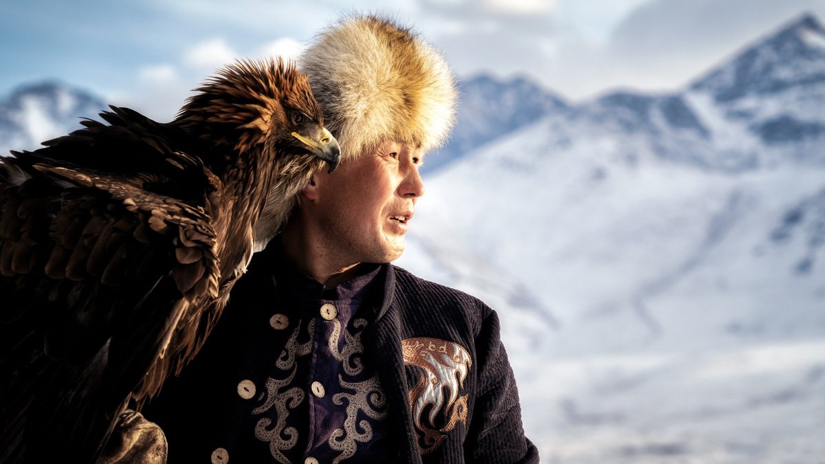 Ruslan, the champion Kyrgyz eagle hunter, stares off into the distance with his golden eagle, Karakuz.